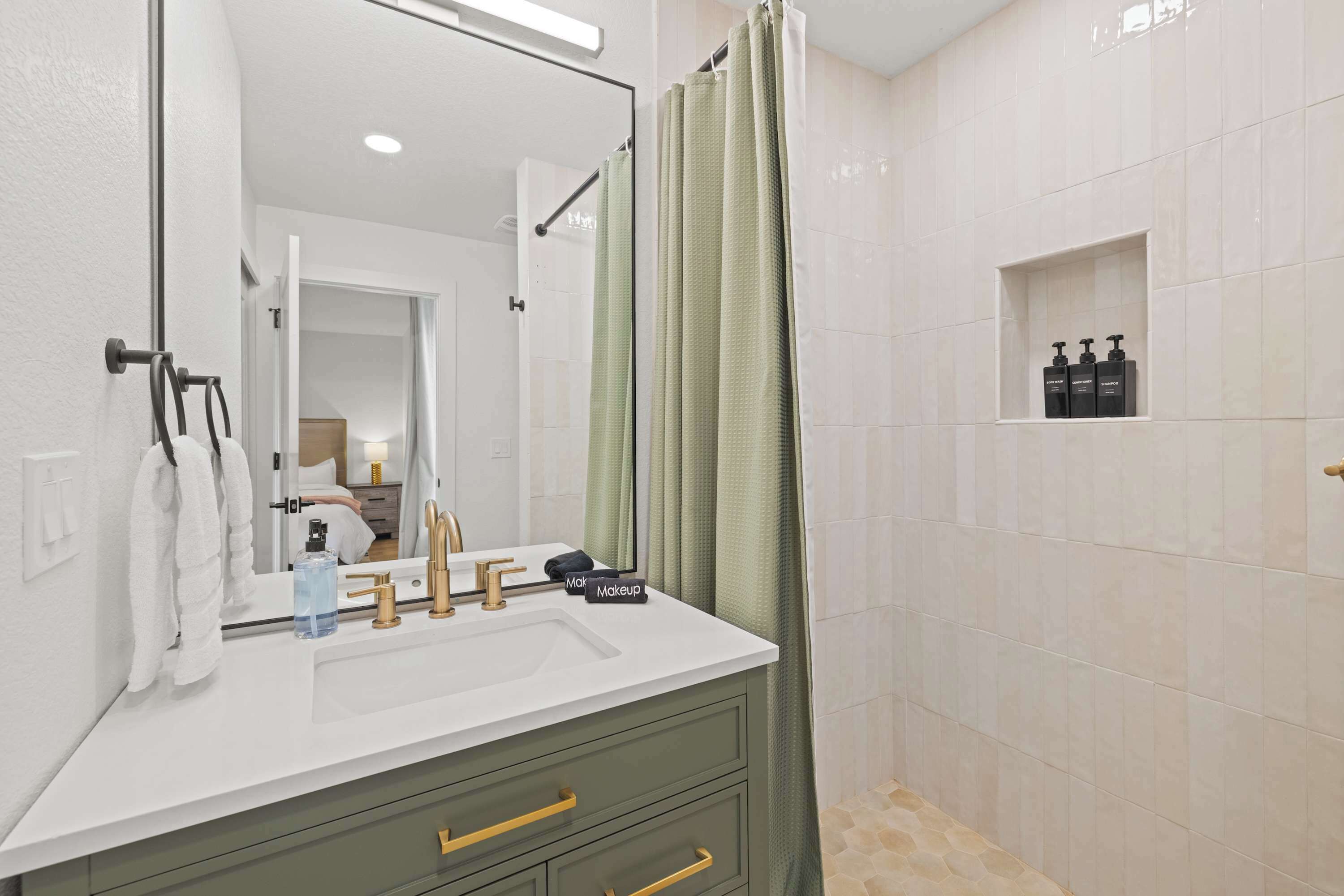 A bathroom with a white sink, gold faucets, a green shower curtain, and a mirror.