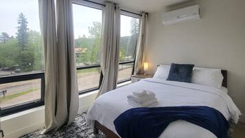 A bedroom with a large bed, a view of the outdoors, and an air conditioning unit on the wall.
