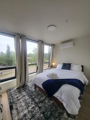 A bedroom with a large bed, a view of the outdoors, and an air conditioning unit on the wall.
