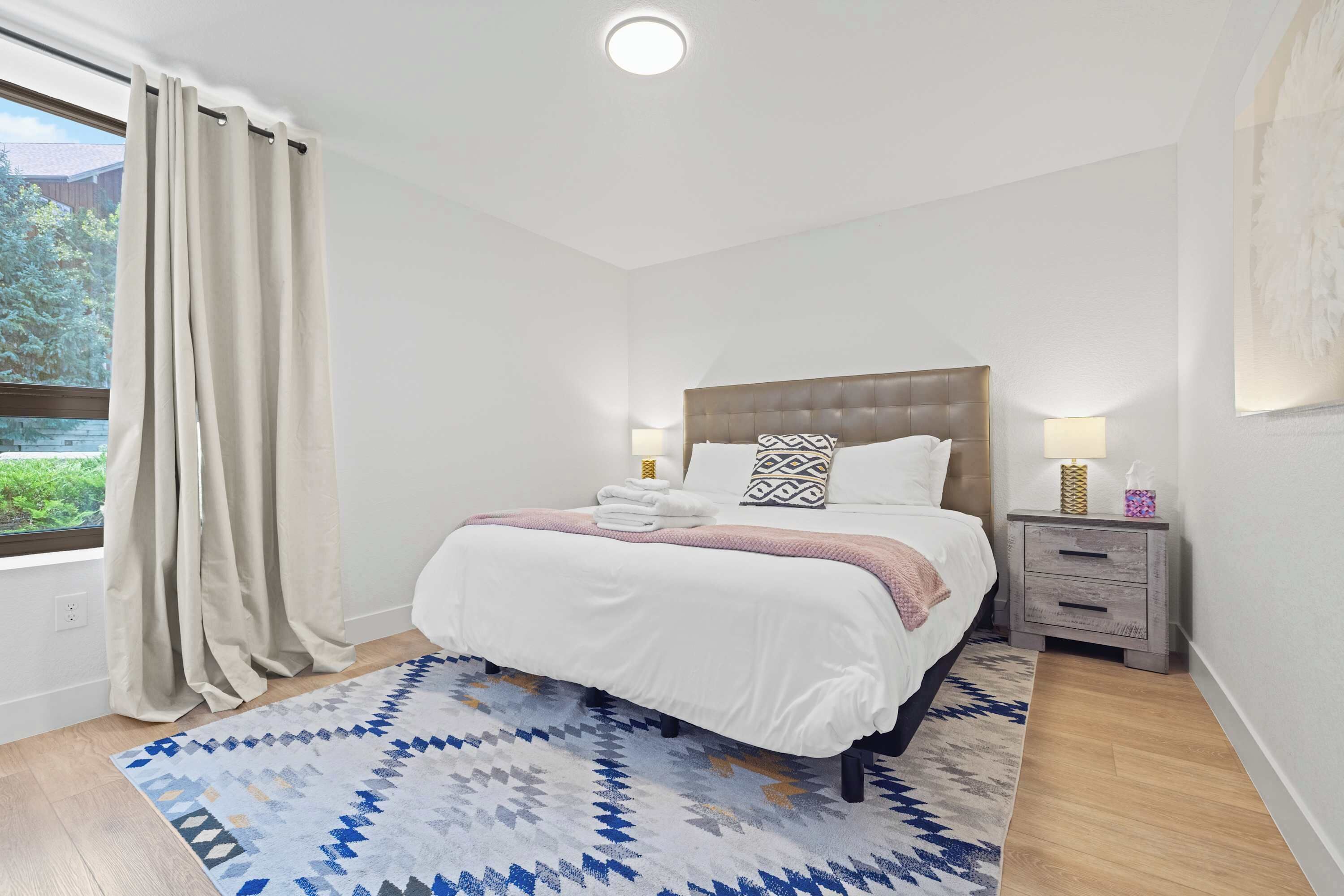 Une chambre à coucher avec un lit, des tables de chevet, un tapis et une fenêtre avec des rideaux.