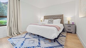Una camera da letto con un letto, comodini, un tappeto e una finestra con tende.