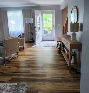 Ein Zimmer mit Holzboden, einer Couch, einer Lampe, einer Bank und einer Tür, die nach draußen führt.