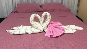 Een bed met een roze sprei en een handdoek gevouwen in de vorm van een hart.