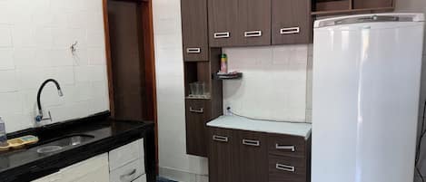 A kitchen with a black countertop, white cabinets, a white refrigerator, and a wooden door.