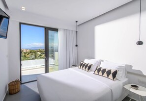 A modern hotel room with a large bed, a small bedside table, a chair, a large window with a view, and a balcony. - Luxury 2BR Cretan Villa Near Hersonissos Beaches (Hersonissos)