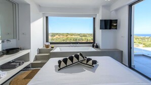 A modern bedroom with a large bed, a built-in sink, a flat-screen TV, and a view of the landscape. - Luxury 2BR Cretan Villa Near Hersonissos Beaches (Hersonissos)