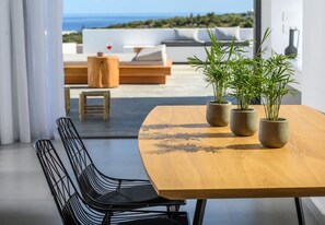 Et moderne spiseområde med et træbord, to plantede planter og udsigt til havet samt en tagterrasse.