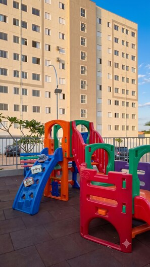 A playground with colorful play structures and a tall residential building in the background. - Apartment 10 minutes from downtown Uberaba! (Uberaba)