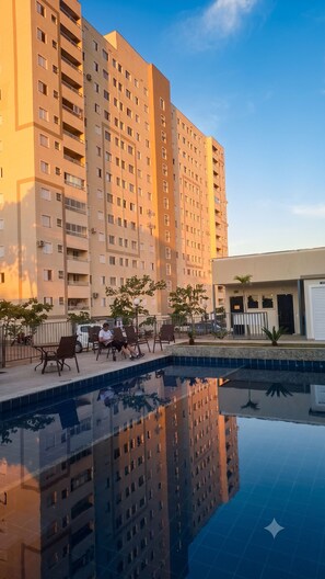 A high-rise building with a swimming pool, outdoor seating, and a clear sky. - Vrbo Property (Uberaba)