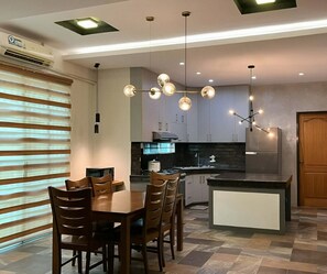 Una cucina moderna con zona pranzo, caratterizzata da un'isola centrale, illuminazione a sospensione e piano cottura integrato.