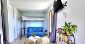 A compact room with a bunk bed, a sofa, a small table with a plant, a shelf with books, and a window with curtains. - L'Atelier - SAINT VERAND (SAINT VERAND)