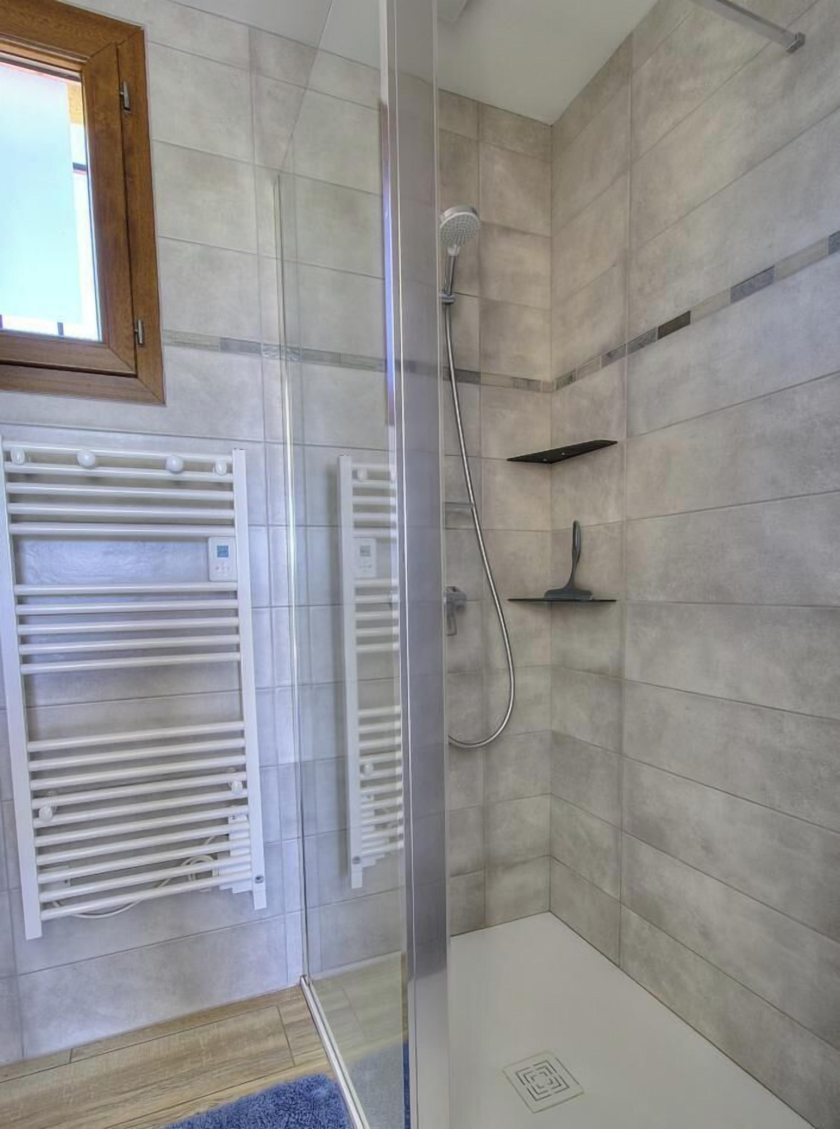 Ein modernes Badezimmer mit Duschkabine aus Glas, integriertem Handtuchhalter und einer kleinen Ablagefläche.