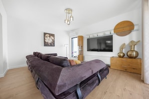 Ein modernes Schlafzimmer mit einem großen Bett, einem Fernseher, einer Holzkommode und einem großen Fenster.