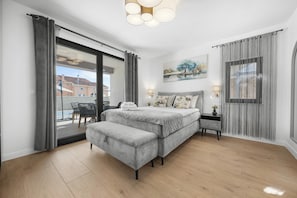 Une chambre à coucher moderne avec un lit, des tables de chevet, un banc, un tableau et une vue sur l’extérieur.
