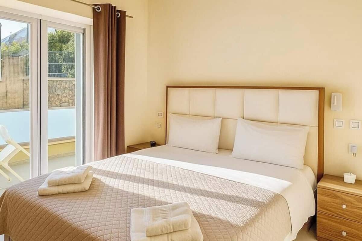 Un dormitorio con una cama grande, una mesita de noche, una puerta corrediza de vidrio y vistas al exterior.