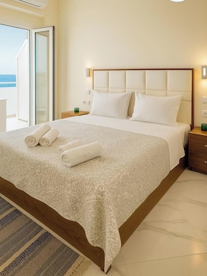 A neatly made bed with a patterned bedspread and pillows, a wooden headboard, and a view of the sea through an open door.