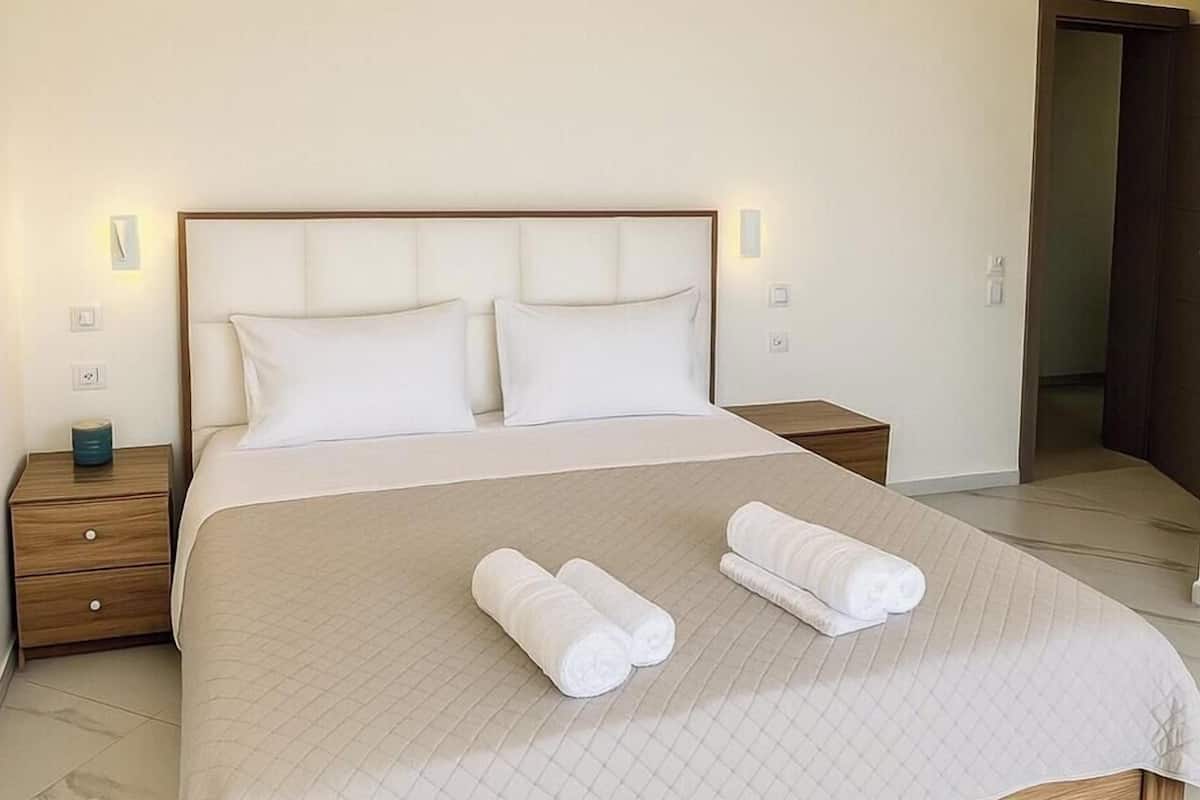 Una habitación de hotel con una cama grande, dos mesitas de noche y una puerta que da a otra habitación.