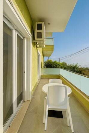 Ein Balkon mit einer Schiebetür aus Glas, einem kleinen Tisch mit zwei Stühlen und einer Wandklimaanlage.