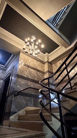 Una escalera de mármol con candelabro, barandillas de metal y vistas al piso superior.