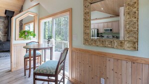 A dining area with a wooden table and chairs, a large mirror with a geometric frame, and a view of a kitchen through an open door.