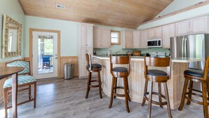 A kitchen with wooden cabinets, a stainless steel refrigerator, and a bar area with stools.