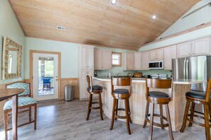 A kitchen with wooden cabinets, a stainless steel refrigerator, and a bar area with stools.