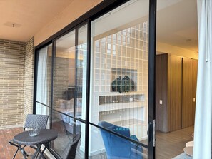 Ein modernes Interieur mit Glastrennwand, einem blauen Stuhl, einem Korbtisch und einer Holztür.