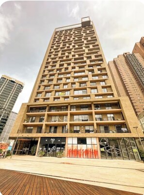 Ein Hochhaus mit mehreren Balkonen, ein Eingangsbereich mit Glasfassade und ein Holzdeck im Vordergrund.