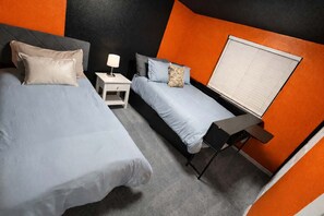 Ein Zimmer mit zwei Betten, einem Nachttisch, einer Lampe und einem Fenster mit Jalousien.