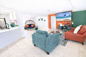 Ein modernes Wohnzimmer mit einer Couch, einem Sessel, einem Couchtisch und einem Gemälde, das eine Strandansicht zeigt.