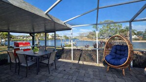 Patio esterno con barbecue, posti a sedere e vista su un lago.
