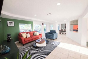 A modern living room with a red sofa, a blue armchair, and a black and white patterned rug. - Breezy Cove-Spacious, Gulf Access, Near Beaches (Apollo Beach)