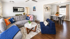 Een woonkamer met een grijze bank, een blauwe fauteuil en een ronde salontafel.