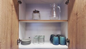 A wooden cabinet with shelves containing glass jars, plates, and ceramic mugs. - A fully furnished, modern, comfortable, and cozy apartment. (Cusco)