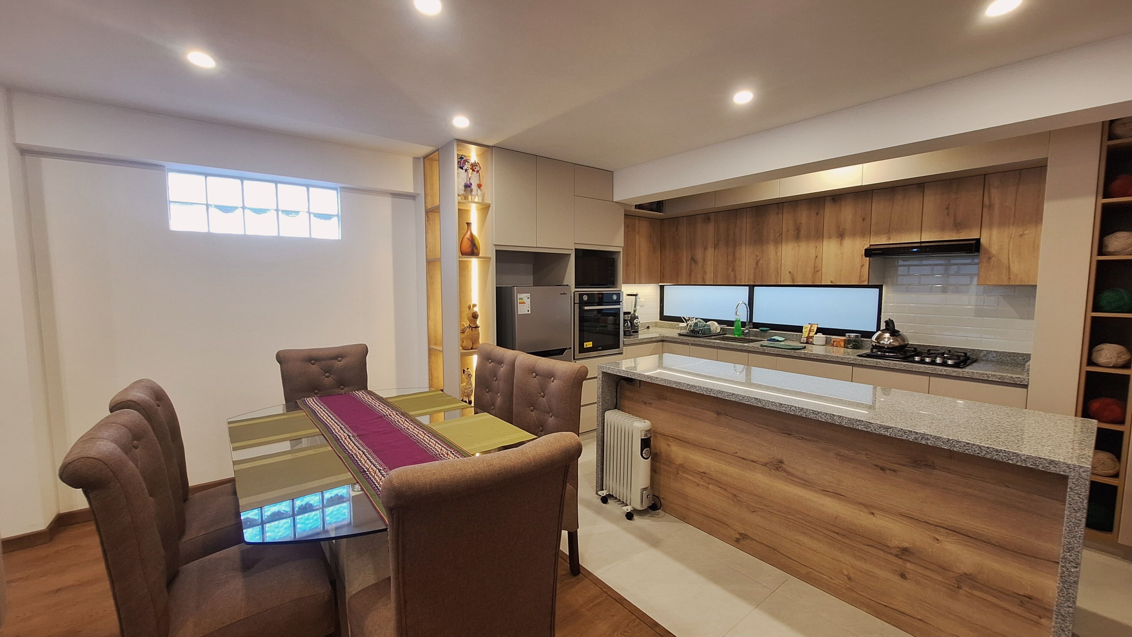 A modern kitchen with a dining area, wooden cabinets, a built-in oven, and a large window.