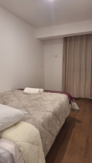 Ein Schlafzimmer mit einem Bett, einem Fenster mit Vorhängen und einem Holzboden.