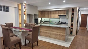 A modern kitchen with a central island, built-in appliances, and a dining area with a glass table and cushioned chairs. - Fully furnished, modern, comfortable, and cozy apartment. (Cusco)