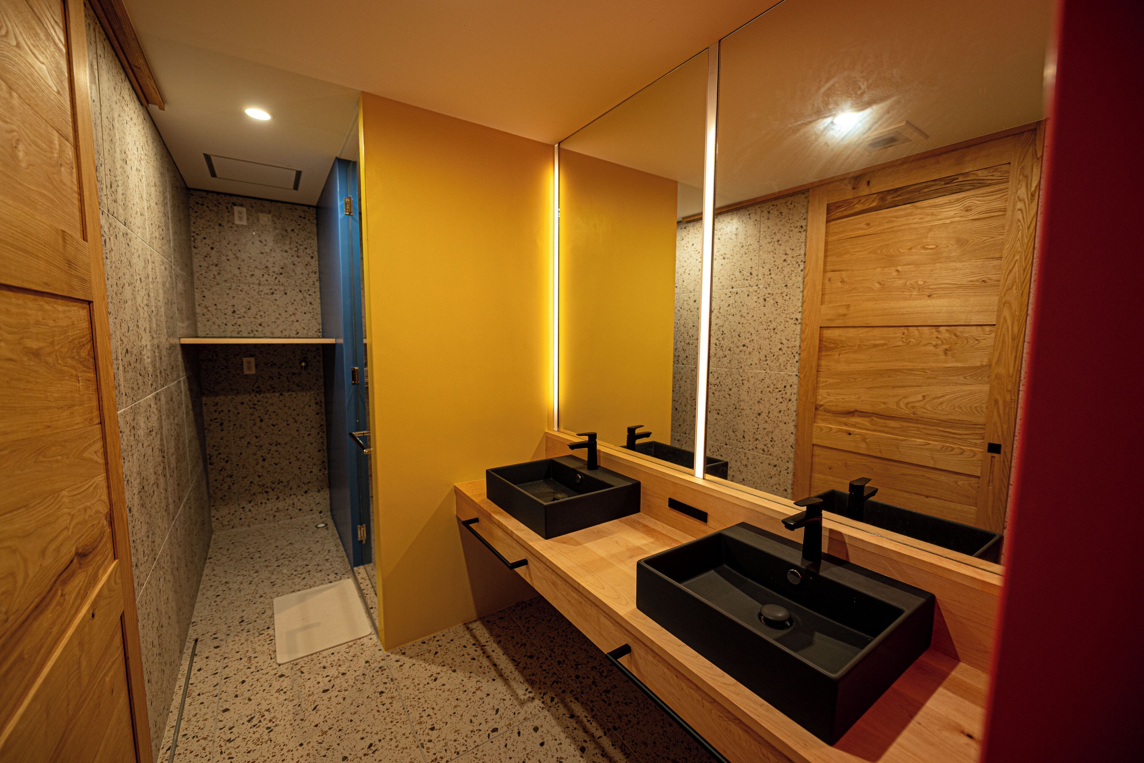 A modern bathroom with two black sinks, a wooden vanity, a mirror, and a shower area.