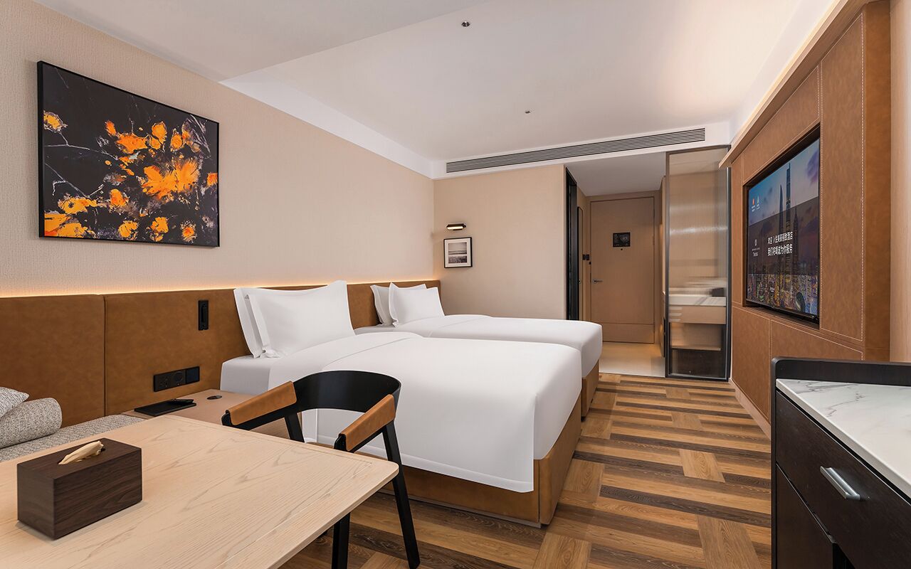 Habitación de hotel con cama, escritorio, silla, televisor y un cuadro en la pared.