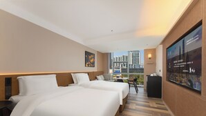 Habitación de hotel con dos camas, un escritorio, una silla, un televisor y vistas a la ciudad.