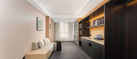 A modern hotel room with a sofa, a small table, a washing machine, and a dark wooden cabinet.