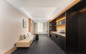 A modern hotel room with a sofa, a small table, a washing machine, and a dark wooden cabinet. - MEHOOD LESTIE Hotel Qingdao Vientiane (Qingdao)