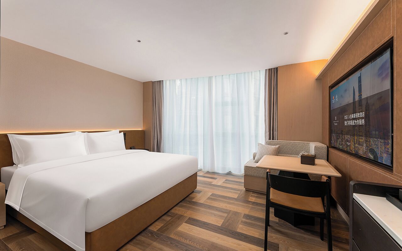Habitación de hotel con cama, escritorio, silla, televisor y ventana con cortinas.