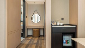 Un baño moderno con suelo de madera, un espejo redondo, un lavabo, un refrigerador pequeño y un cubo de basura.