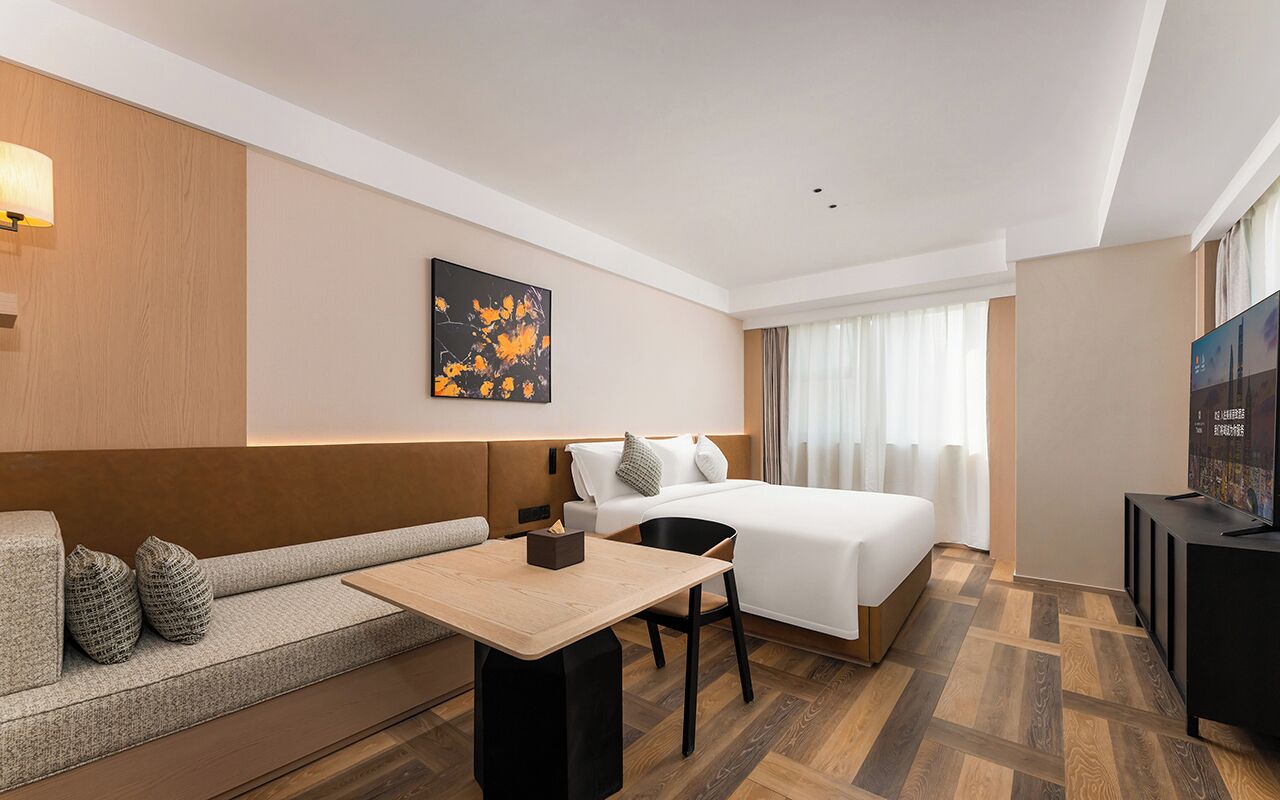 A hotel room with a bed, a sofa, a table, a TV, and a painting on the wall.