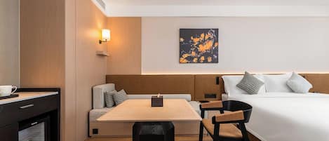 Una habitación de hotel moderna con cama, escritorio, silla, mesita, sofá y una obra de arte colgada en la pared.