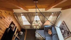 Una habitación acogedora con techo de madera, un sofá con cojines, una lámpara colgante y una chimenea.