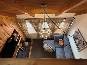 Ein gemütliches Zimmer mit Holzboden, einer Couch mit Kissen, einer Pendelleuchte und einem Kamin.