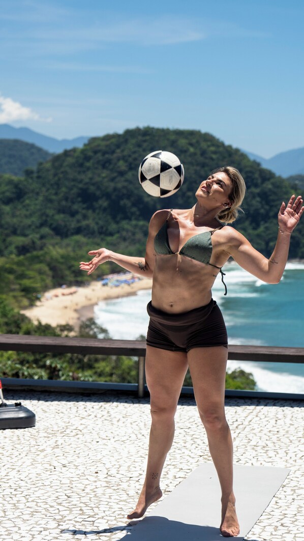 A person juggling a soccer ball on a balcony overlooking a beach and ocean.