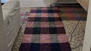 A bedroom with a bed, a small table, a colorful rug, and a view of a beach and mountains.